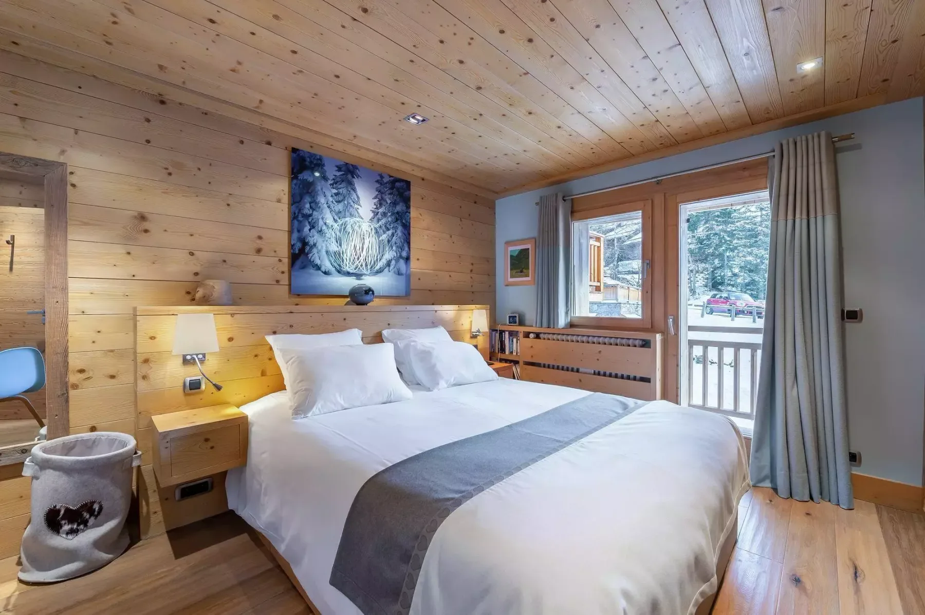 Un dormitorio con una cama bien hecha y ventanas con vistas a una zona arbolada.
