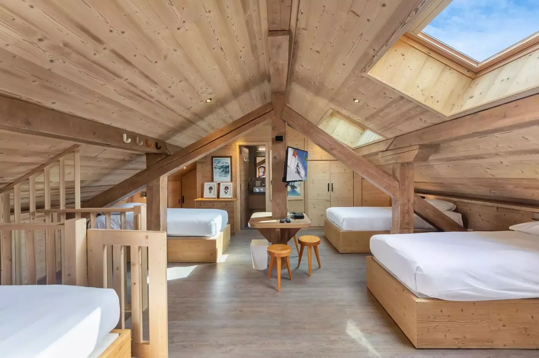 Un dormitorio abuhardillado revestido de madera, con varias camas y tragaluces.