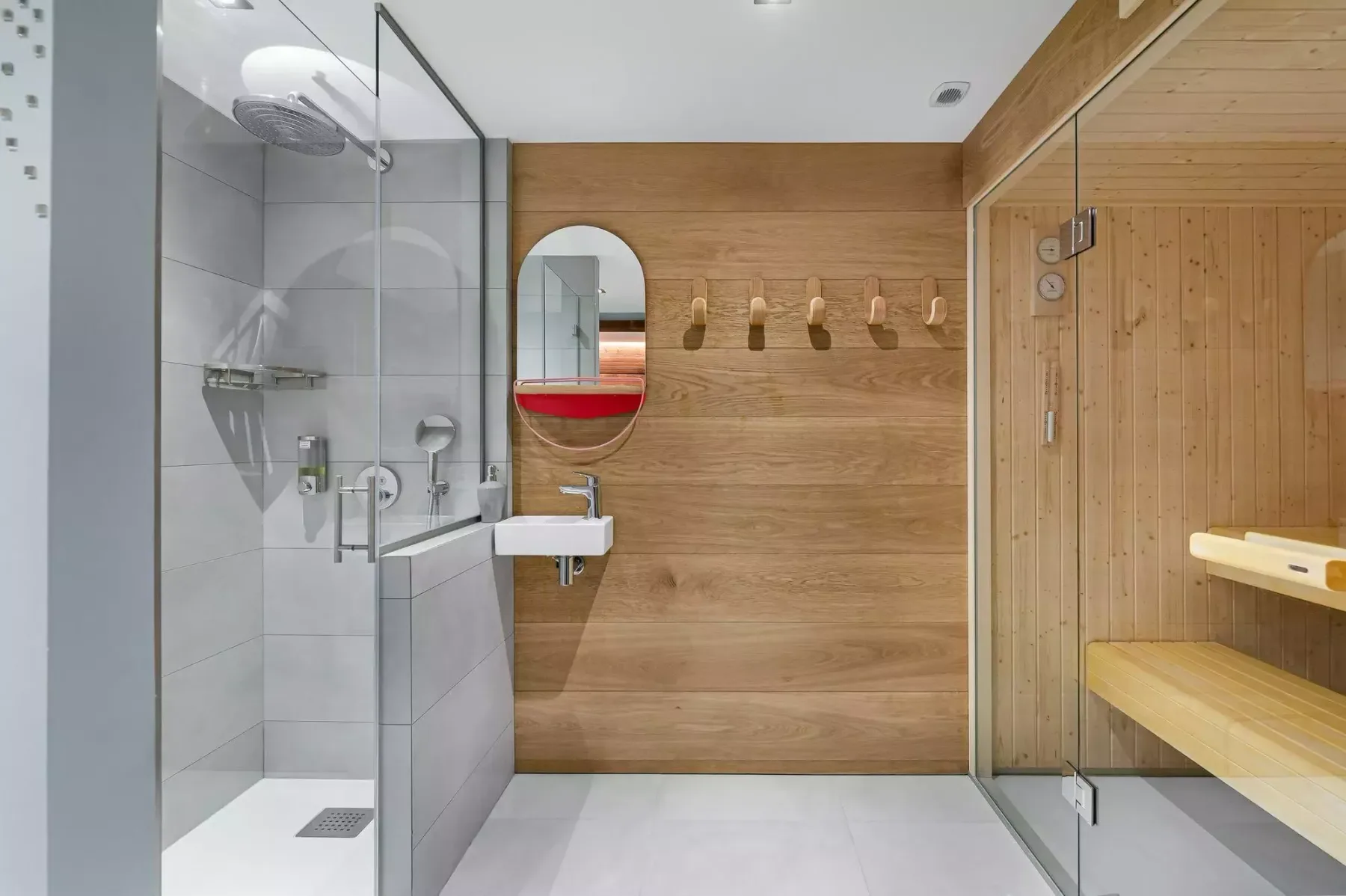 Un baño moderno con ducha de vidrio, lavabo suspendido y sauna de madera.