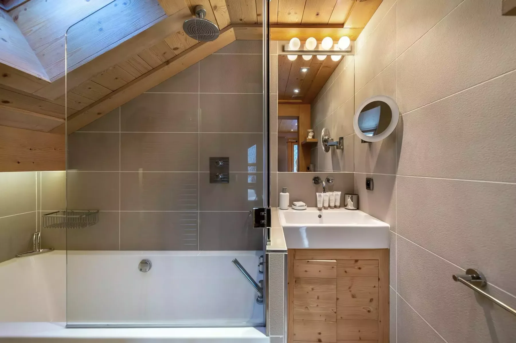 Un baño con bañera, lavabo y techo inclinado de madera.