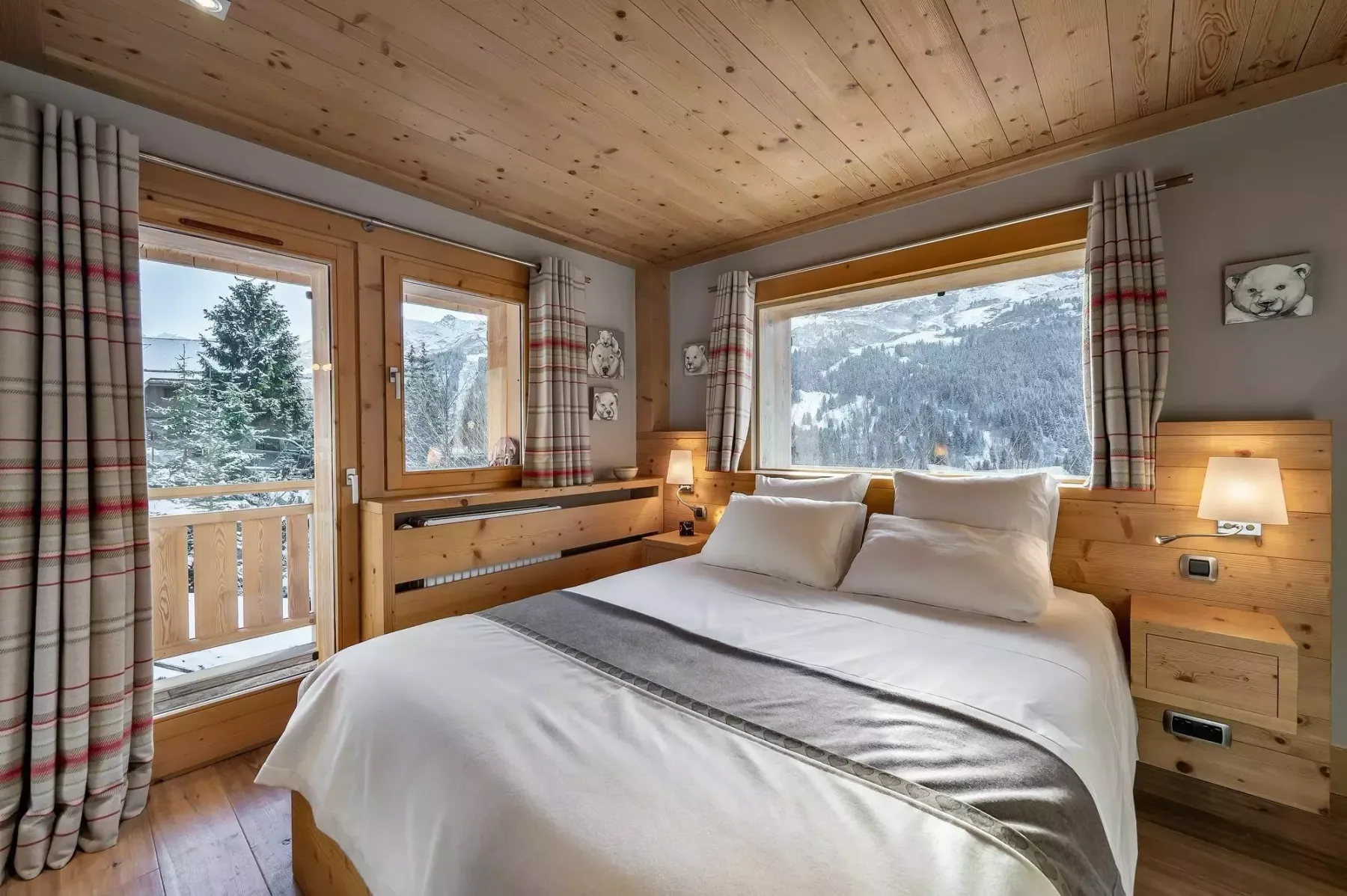 Dormitorio con una cama doble, muebles de madera y grandes ventanas con vistas a un paisaje montañoso.