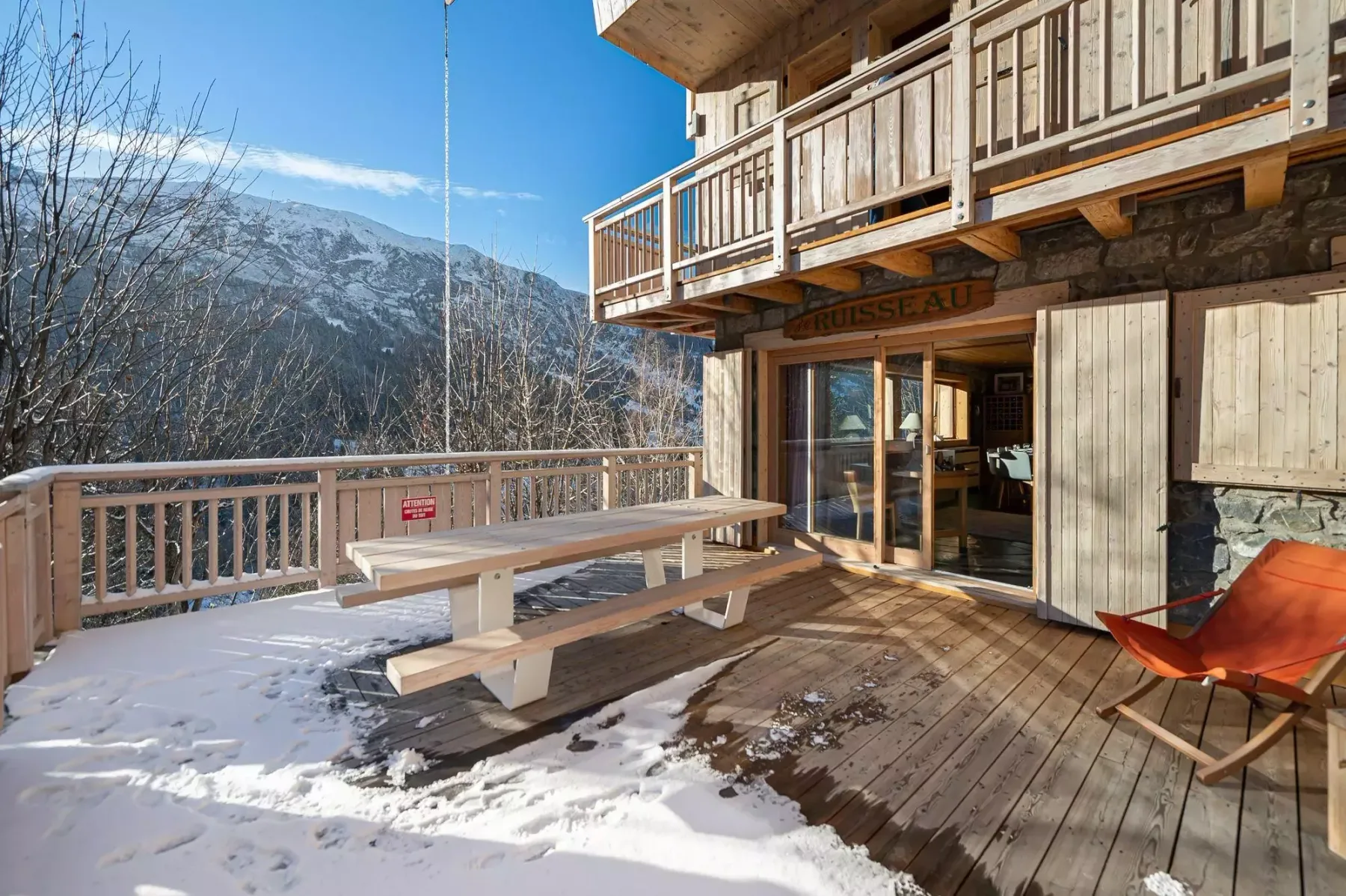 Una terraza de madera con una mesa de picnic da a un paisaje montañoso nevado.