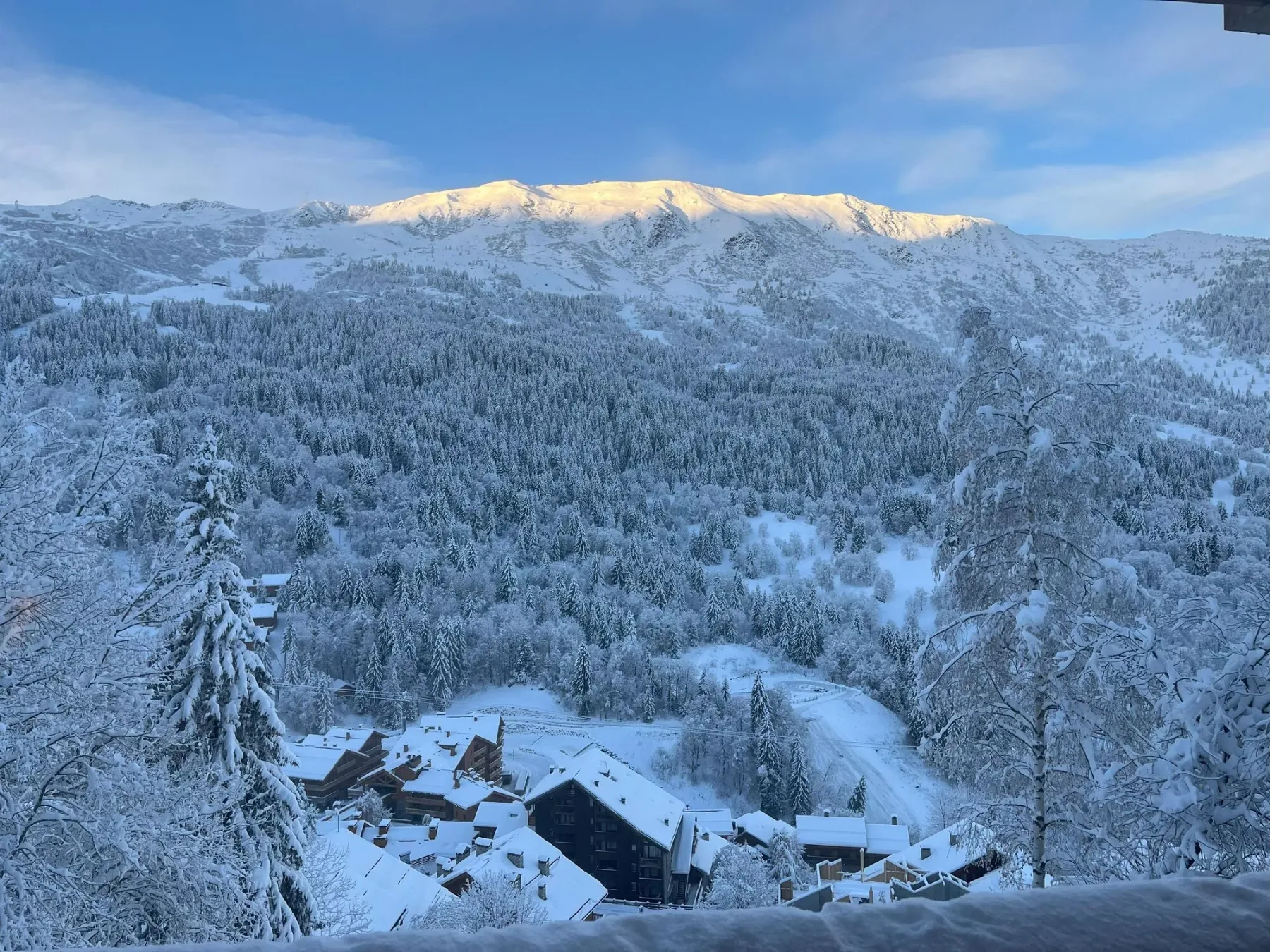 Un paisaje de montaña nevado domina un conjunto de edificios entre laderas boscosas.