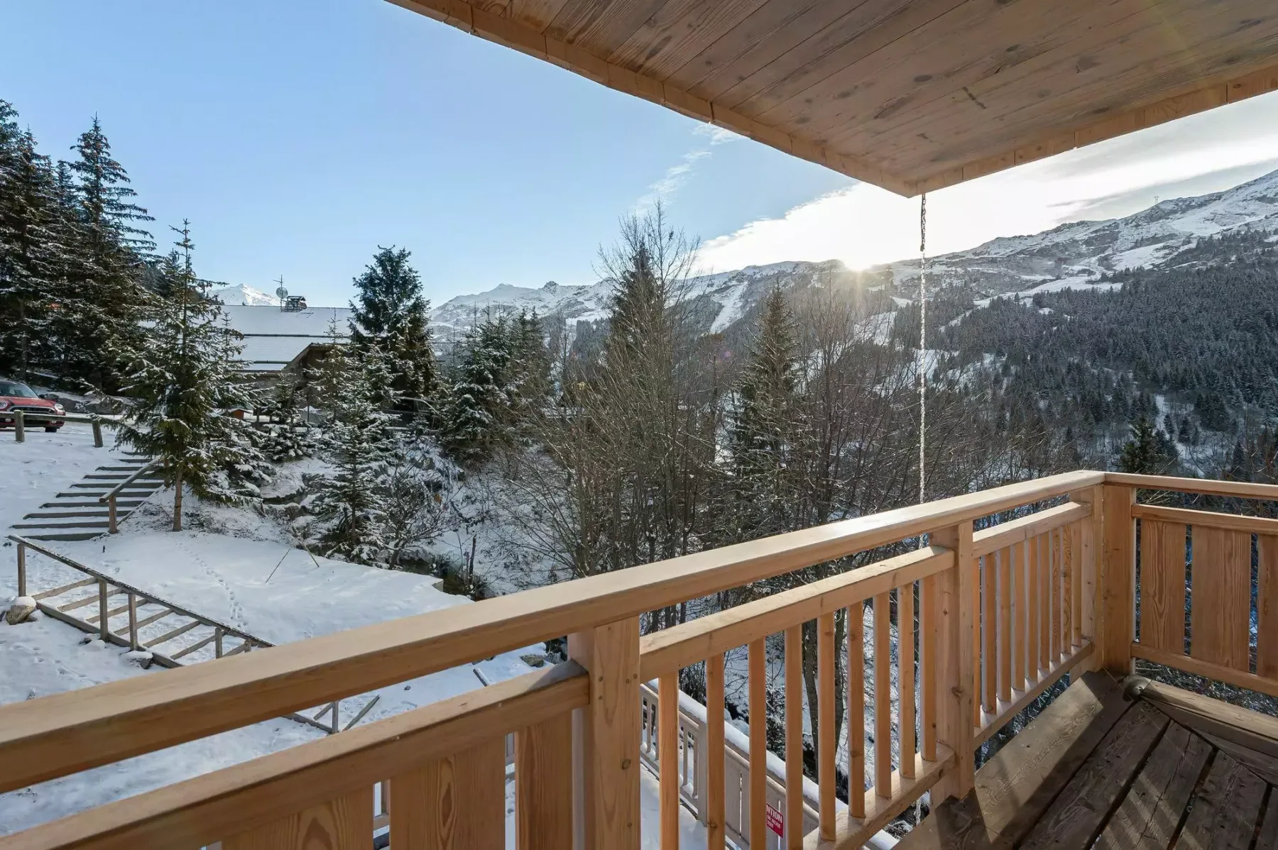 A wooden balcony overlooks a snowy mountain landscape and evergreen trees.