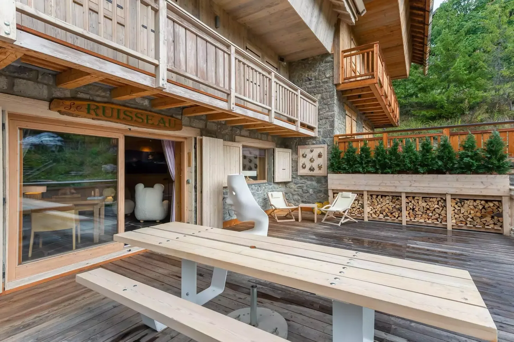 Una terraza de madera con una mesa de picnic y asientos al aire libre junto a un chalet.