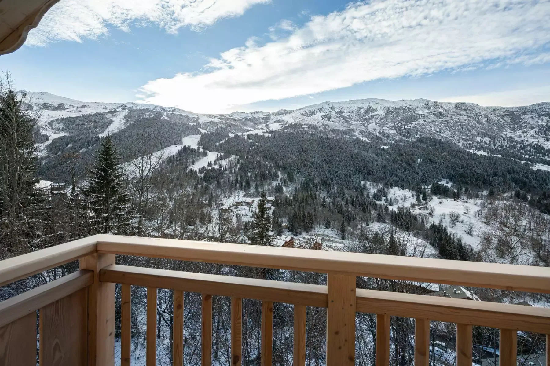 Un balcón de madera da a montañas nevadas bajo un cielo parcialmente nublado.
