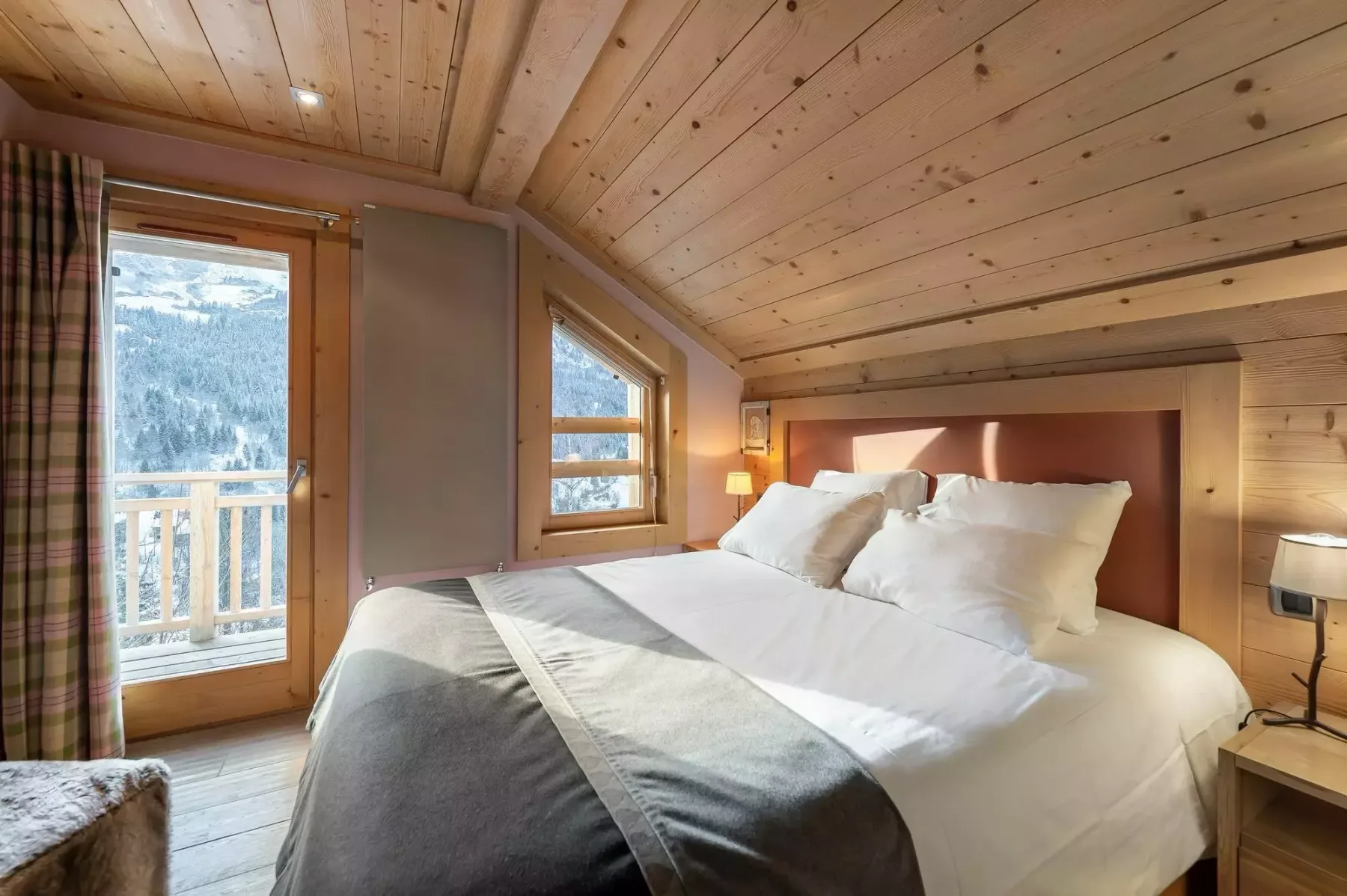 Un dormitorio con una cama bien tendida y una puerta al balcón con vistas a las montañas.