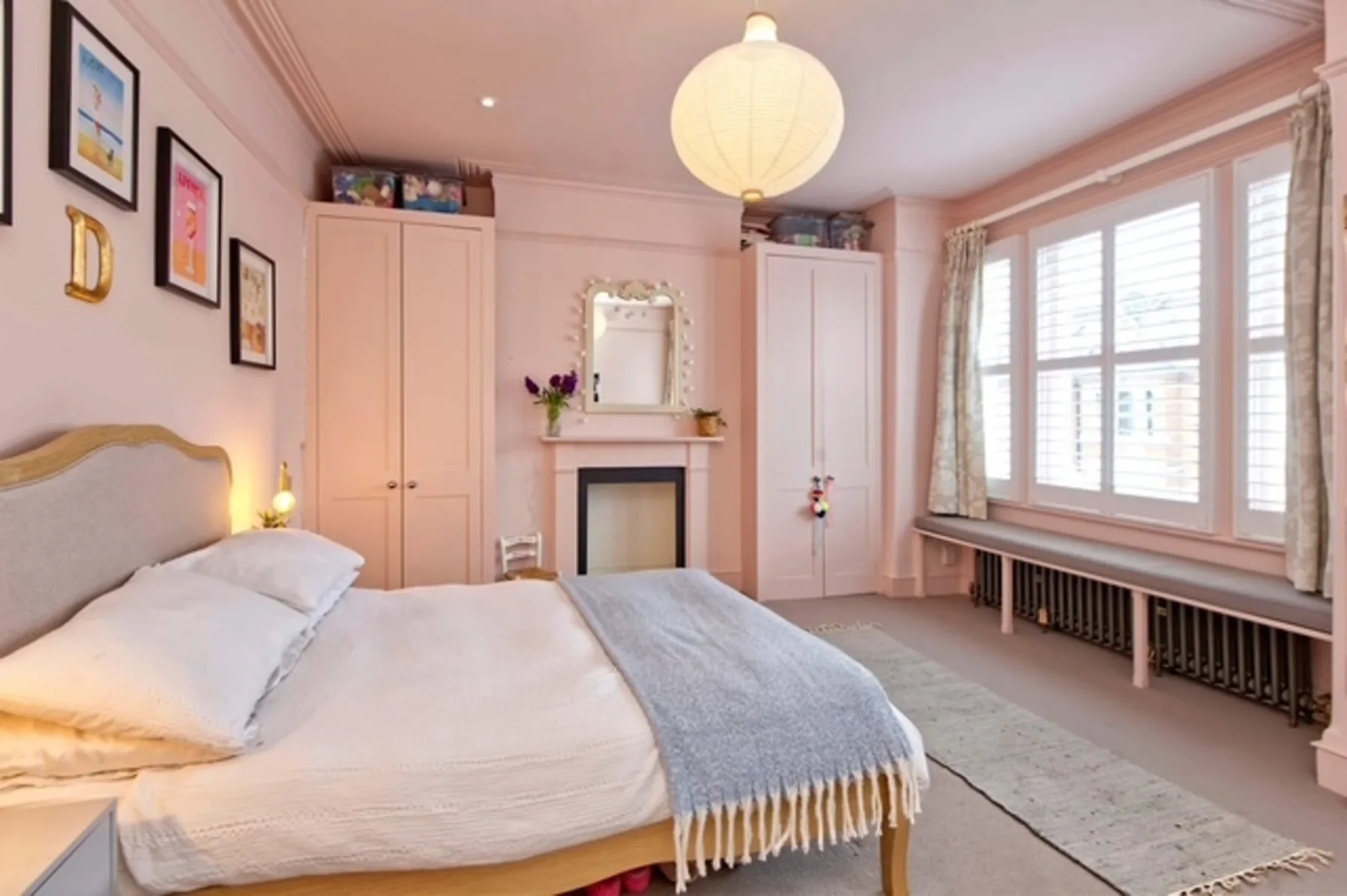 A bedroom with a bed, fireplace, and large shuttered windows.