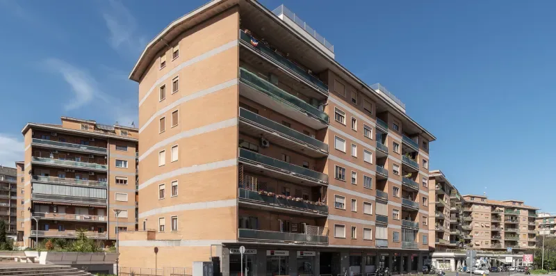 Un edificio de apartamentos de varias plantas con balcones se alza junto a una calle soleada.