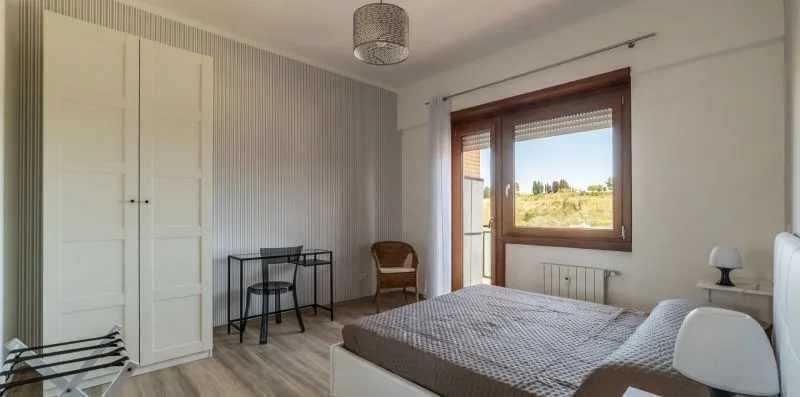 Un dormitorio con una cama, un escritorio pequeño y una ventana con vistas a la vegetación.
