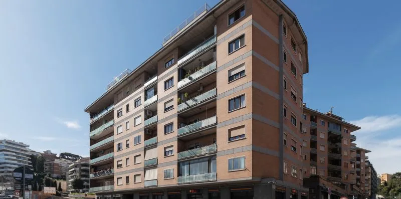 Un edificio de apartamentos de varias plantas con balcones se alza bajo un cielo azul despejado.