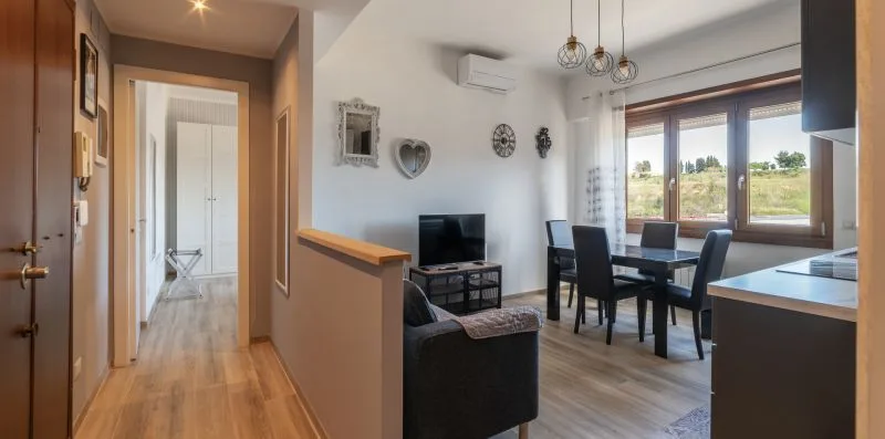 Una zona de comedor y estar con una mesa oscura junto a grandes ventanas.