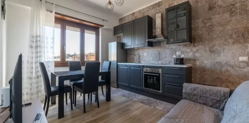 Comedor junto a una cocina compacta, con armarios oscuros y una mesa.