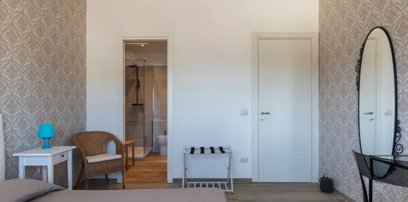 Un dormitorio con papel tapiz estampado, una cama y una puerta abierta hacia un baño.