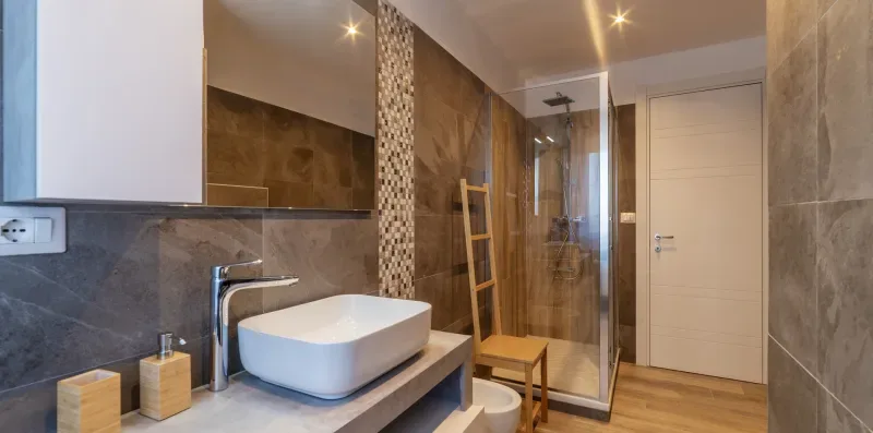 Baño con lavabo sobre encimera, ducha de vidrio y asiento de madera.