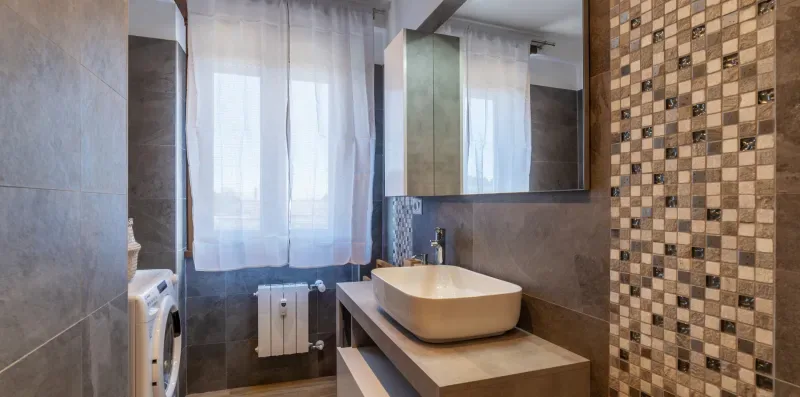 Un baño con un lavabo sobre encimera y una ventana con cortinas translúcidas.