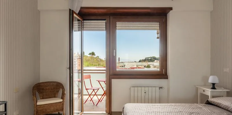 Un dormitorio con una cama junto a una puerta de balcón y una ventana abiertas.