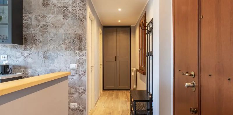 Un pasillo de entrada con una puerta de madera, una pared estampada y armarios.
