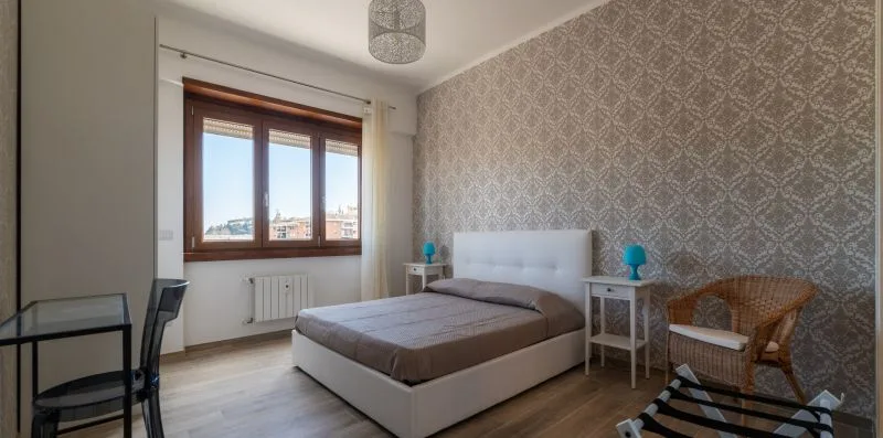 Un dormitorio con una cama, papel pintado estampado y una ventana.