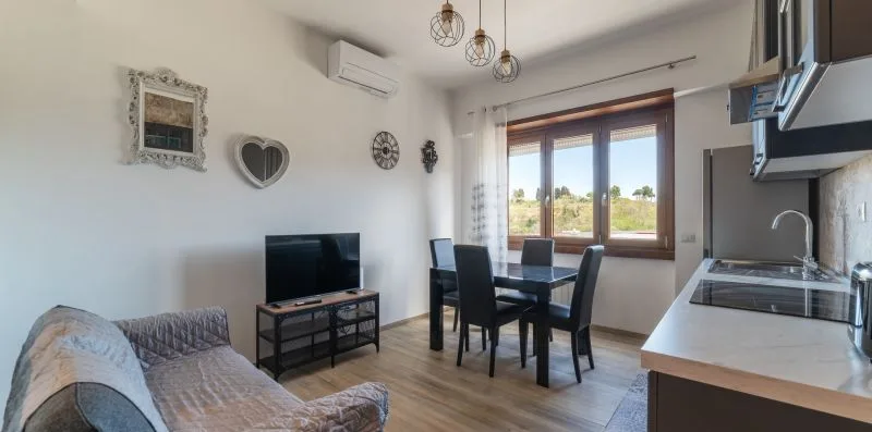 Una zona de estar y comedor con televisión, asientos y una mesa junto a las ventanas.