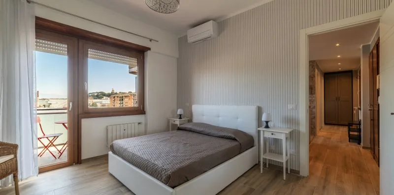 Dormitorio con una cama doble junto a una ventana y una puerta abierta.