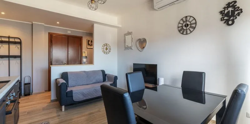 Una zona de estar y comedor con sofá, mesa y televisor en la pared.