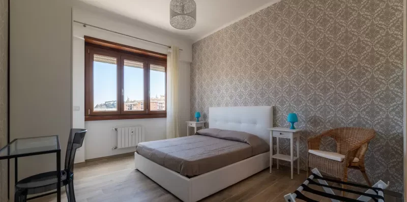 Un dormitorio con una cama doble, papel pintado estampado y una ventana.
