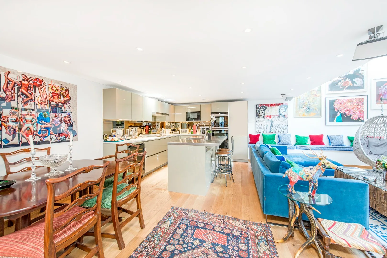 An open-plan living and dining area has colorful artwork and a blue seating arrangement.