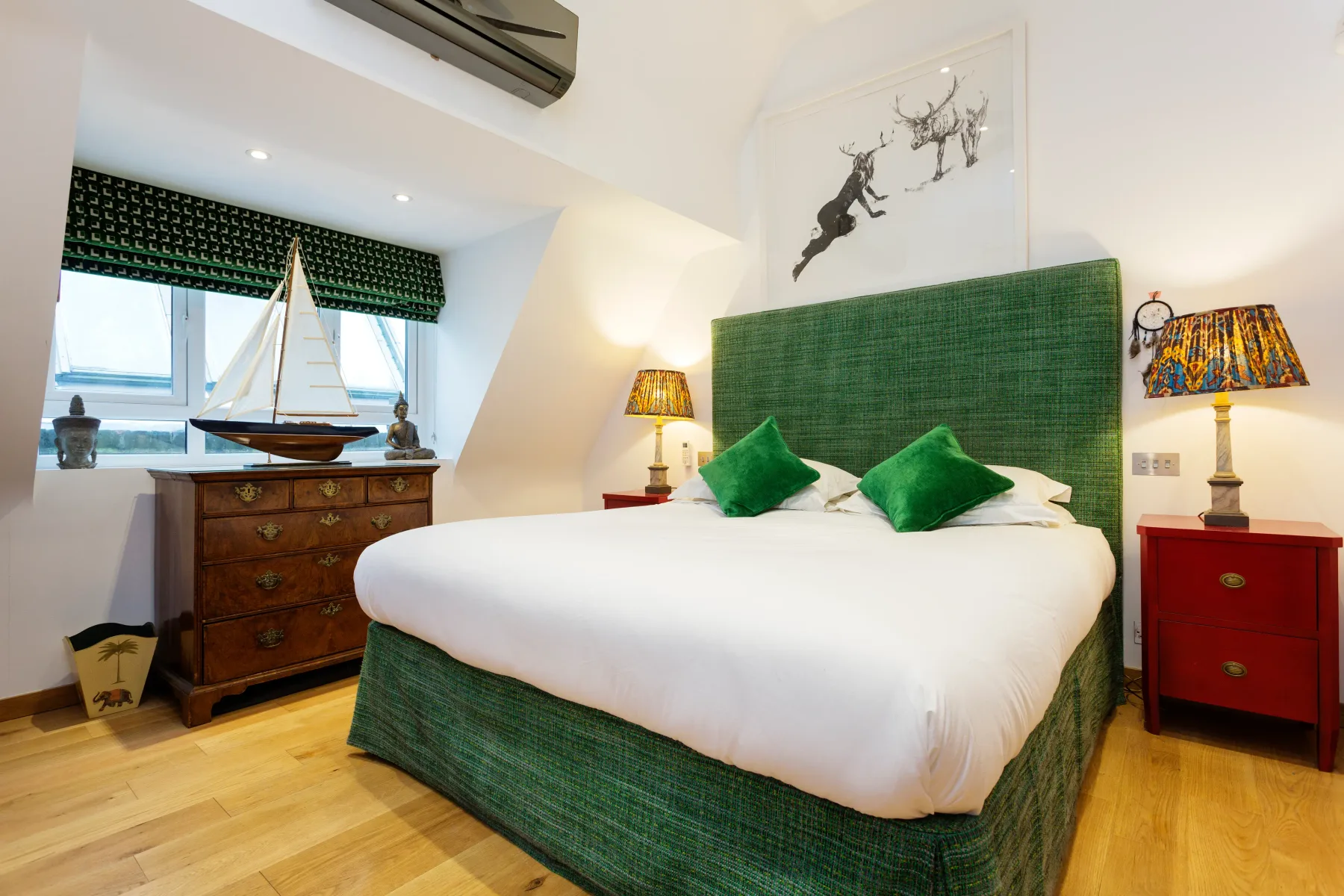 Dormitorio con una cama verde, mesas de noche y una ventana con un modelo de velero.