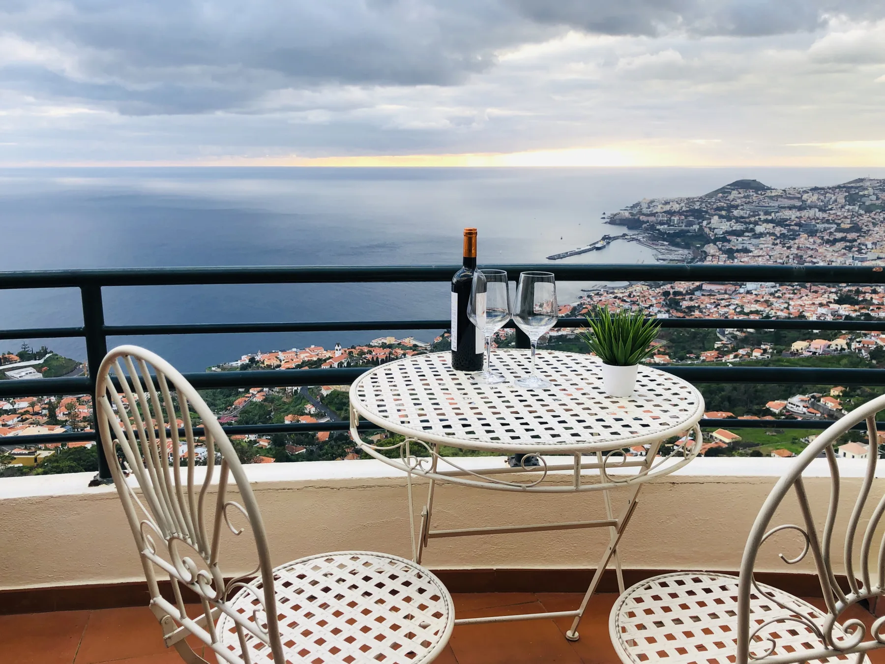 A balcony dining area overlooks the ocean and a coastal hillside.