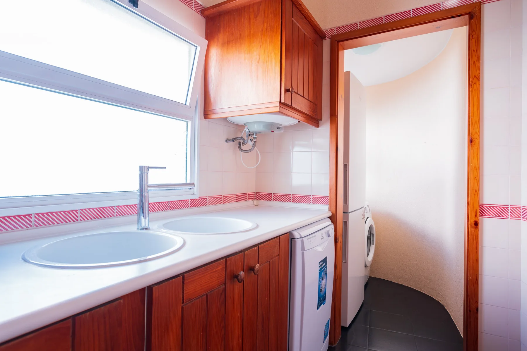 A tiled bathroom with a double sink, wooden cabinetry, and a washing machine.
