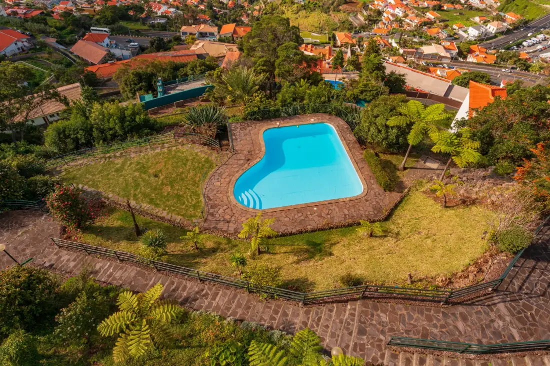 An outdoor swimming pool sits amid landscaped grounds and surrounding homes.
