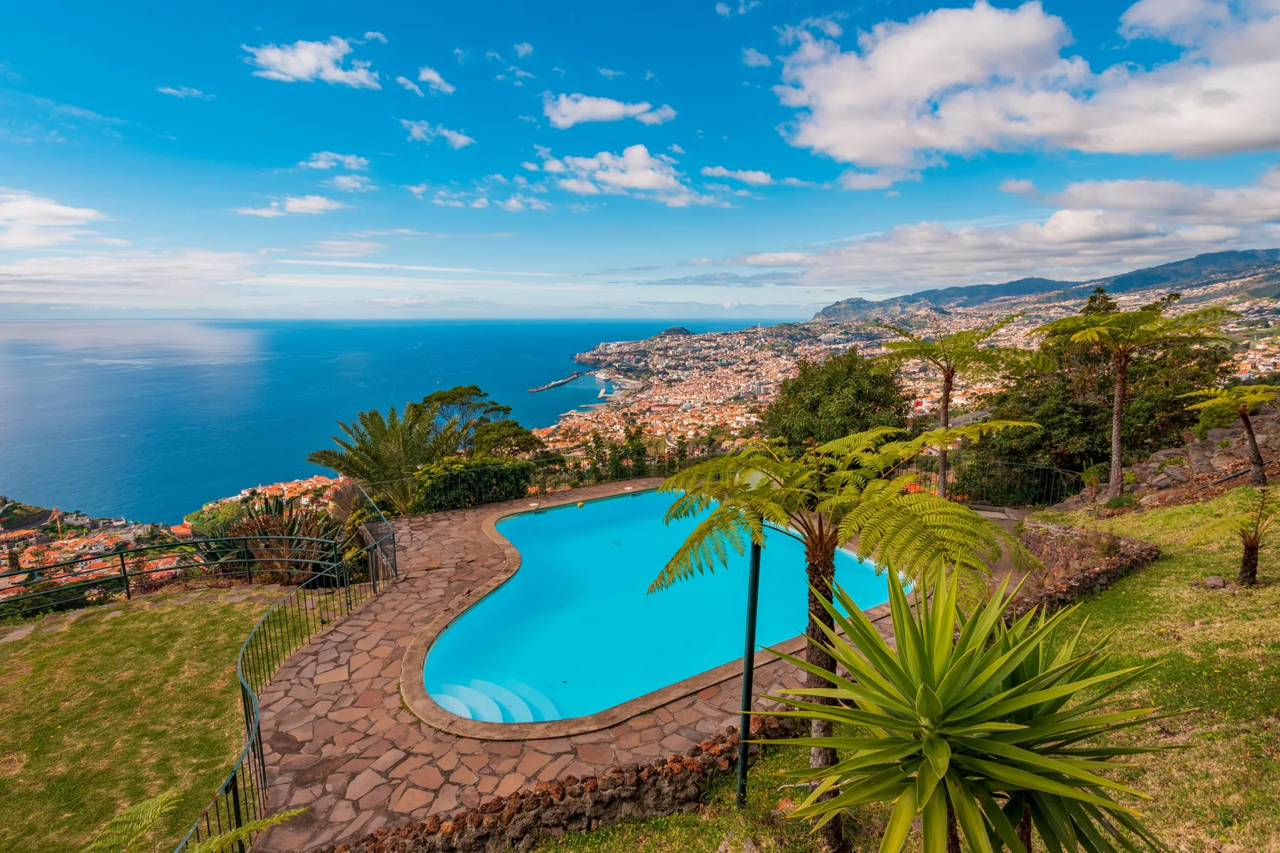 A swimming pool overlooks the ocean and a coastal city.