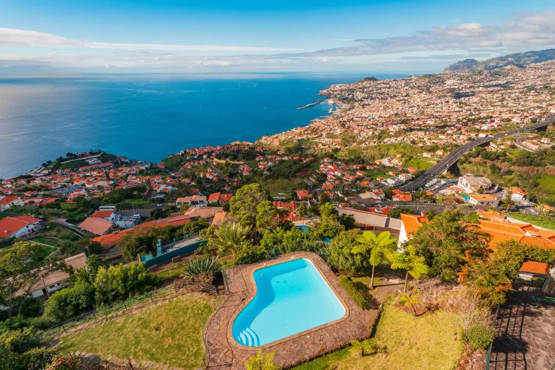A coastal hillside overlooks the ocean, with a swimming pool in the foreground.