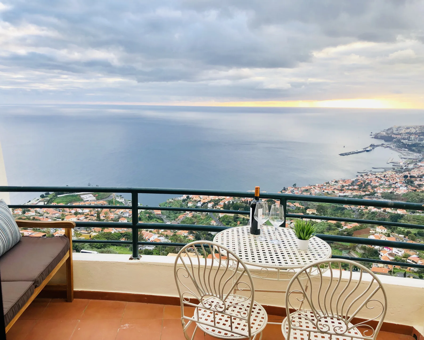 A balcony seating area overlooks the ocean and a coastal town.