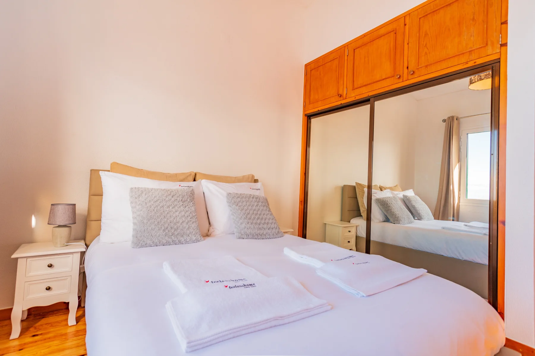A bedroom with a neatly made bed and a mirrored wardrobe.