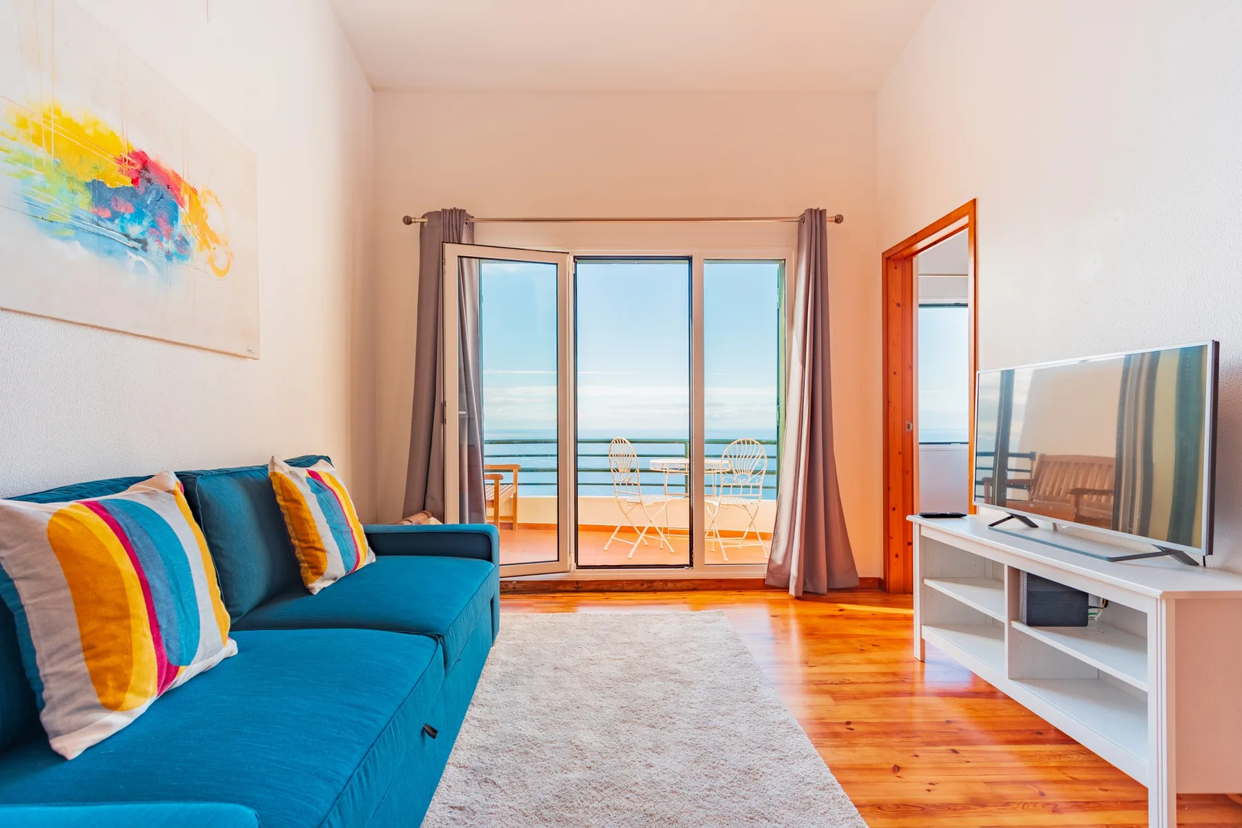 A living room with blue seating, a television, and glass doors overlooking the ocean.