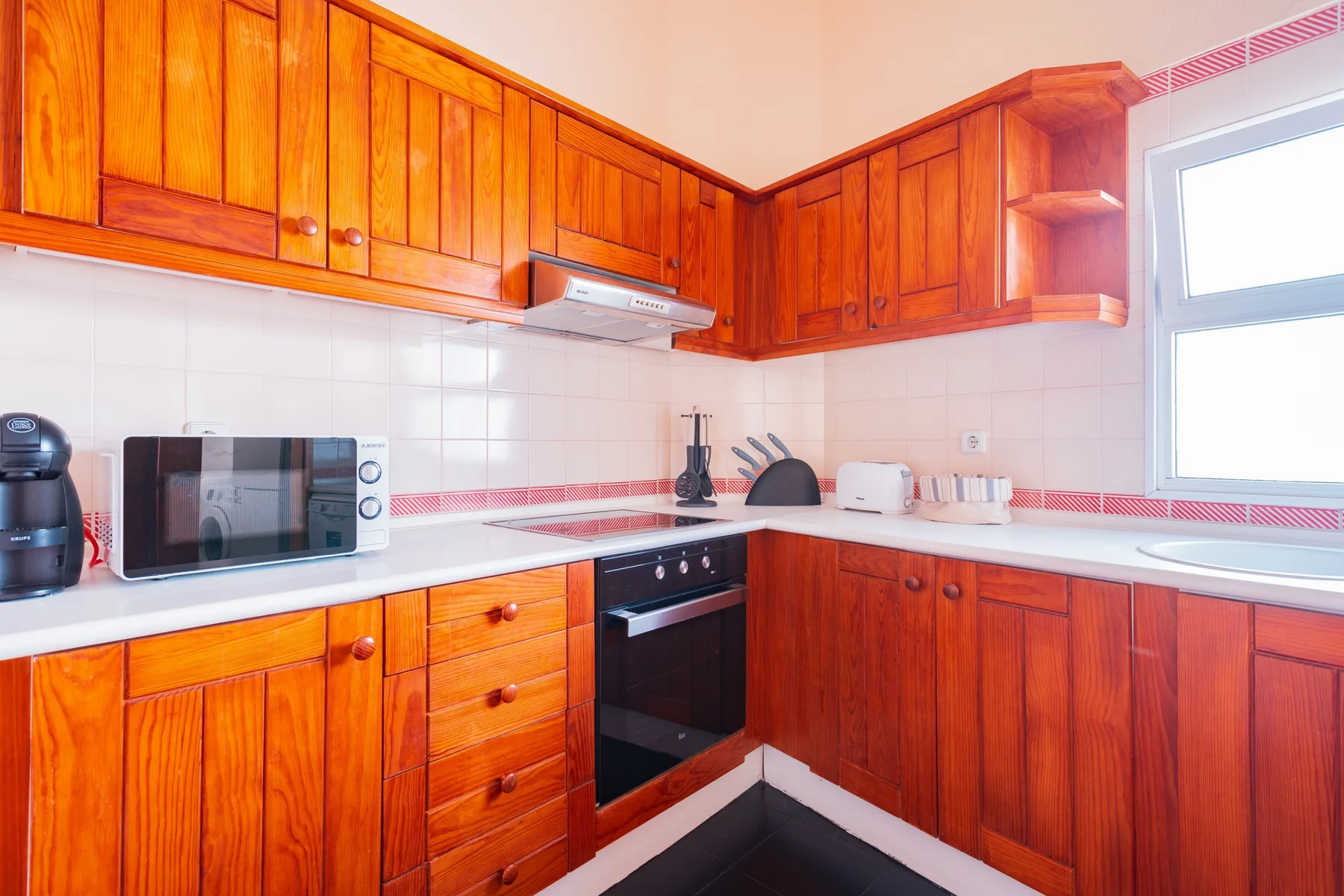 A kitchen with wooden cabinets, a microwave, and a bright window.