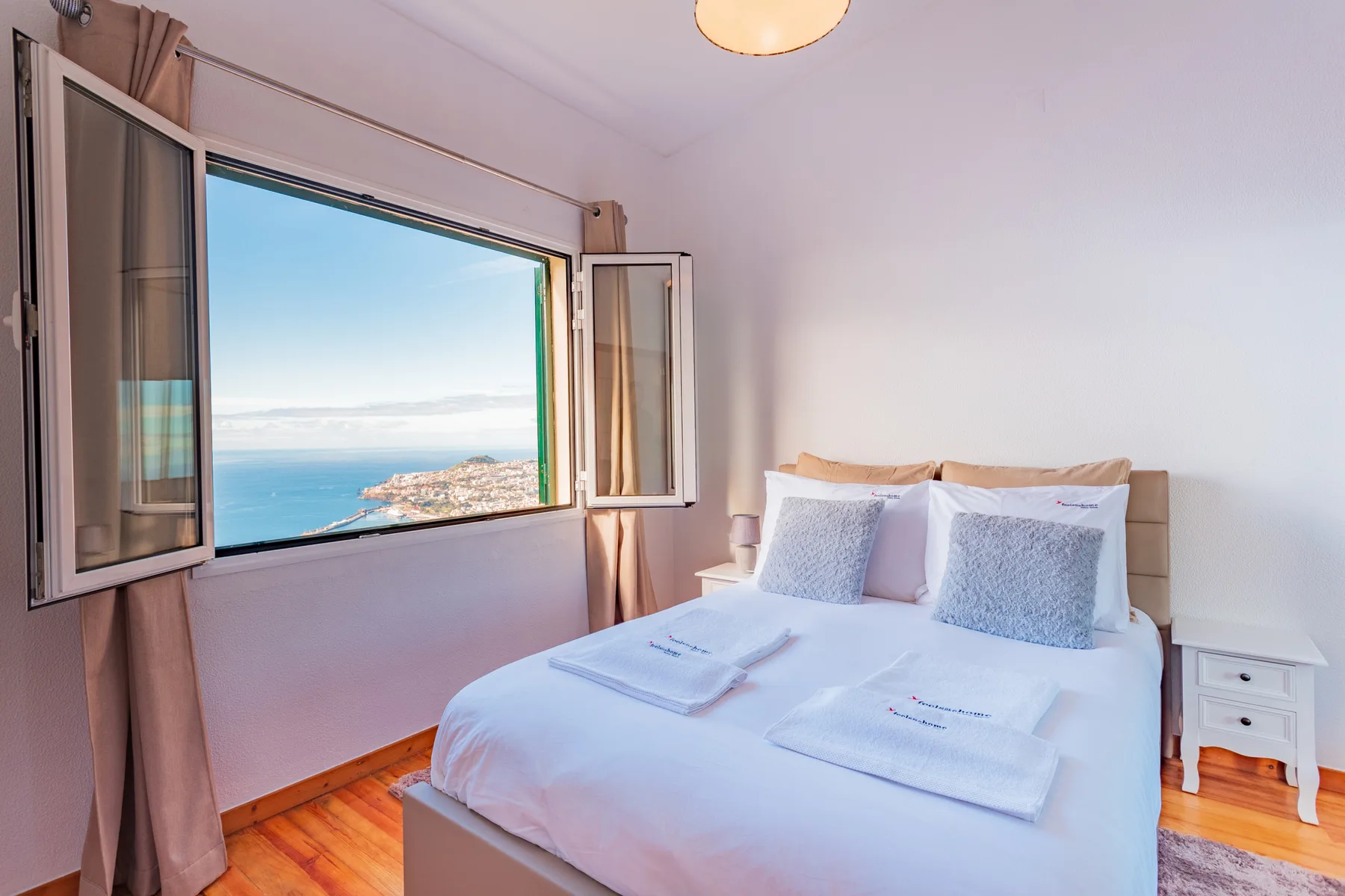 A bedroom with a neatly made bed beside a large window overlooking the sea.