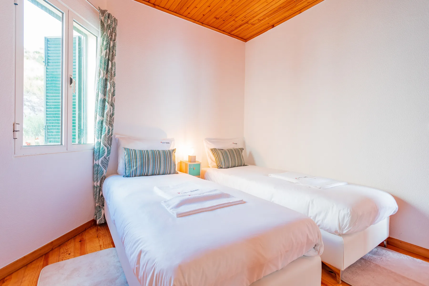 A bright bedroom with two beds beside a window.