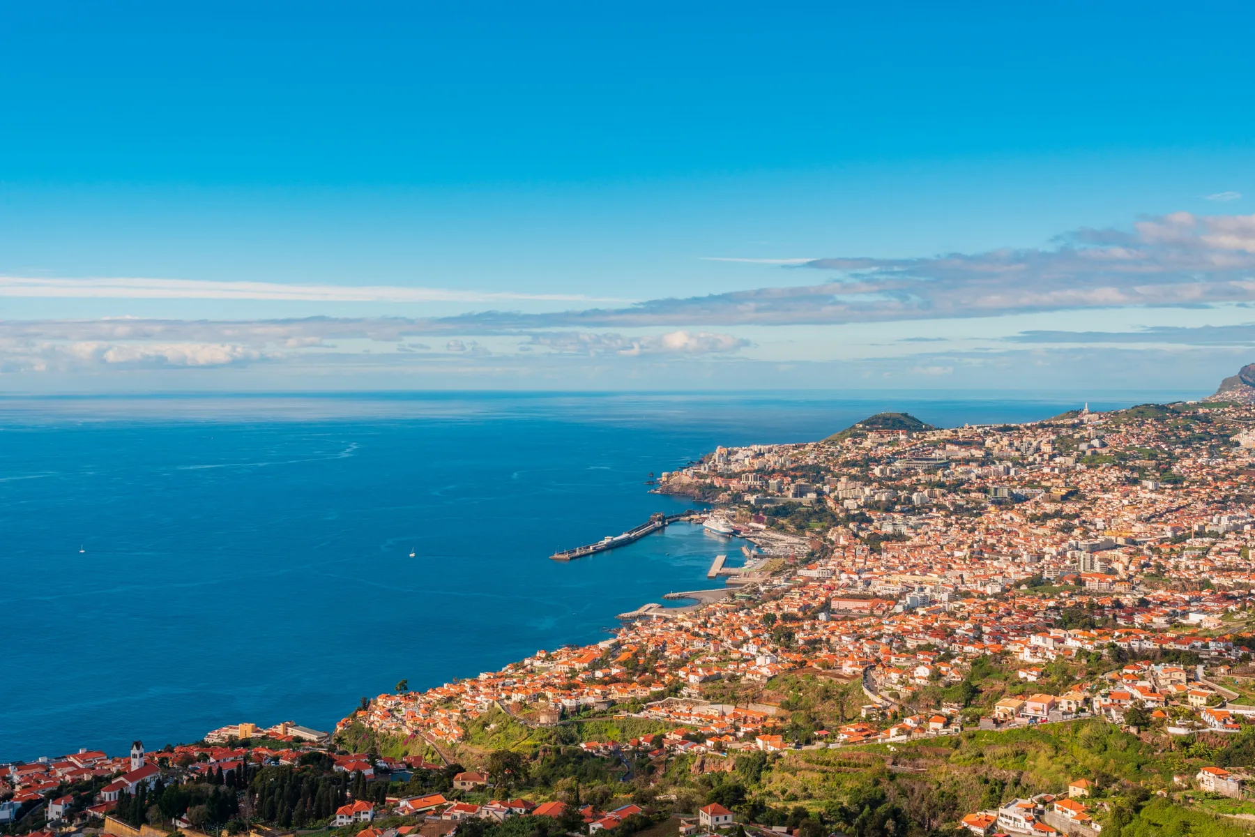 Coastal cityscape with a broad view of the ocean and hillside buildings.