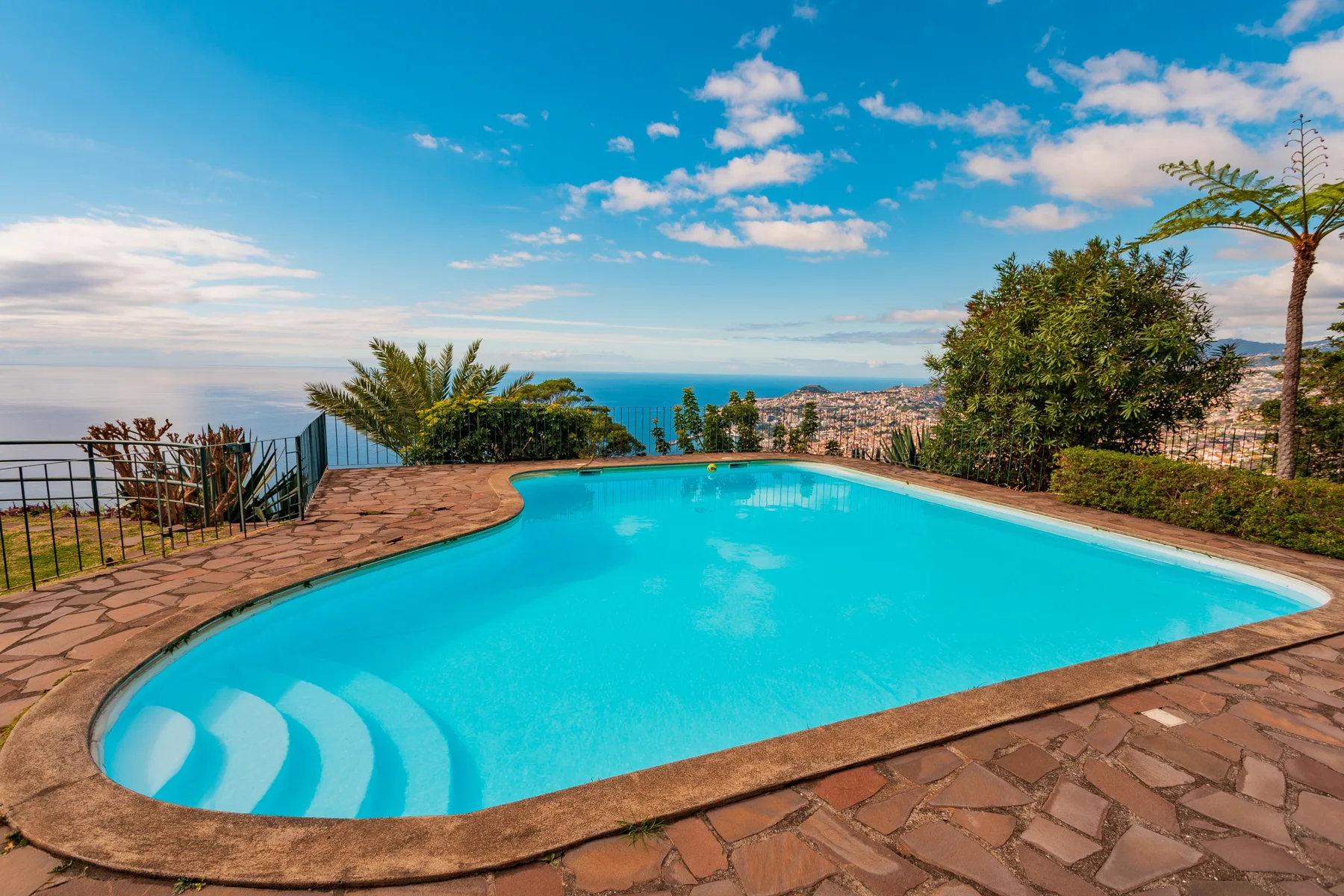 A swimming pool overlooks the ocean and a distant coastal city.