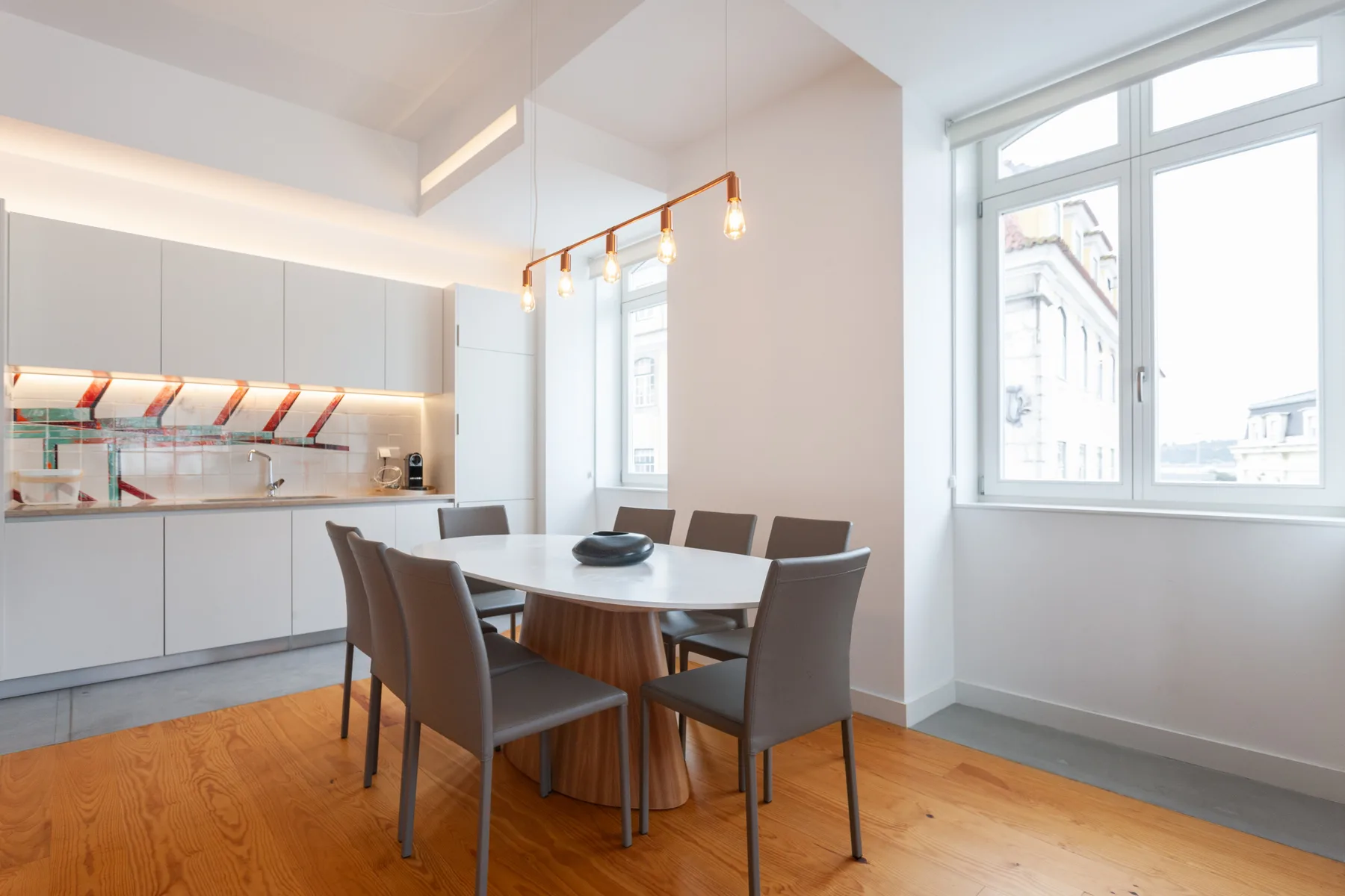 A bright dining area with a table beside a compact kitchen and large windows.