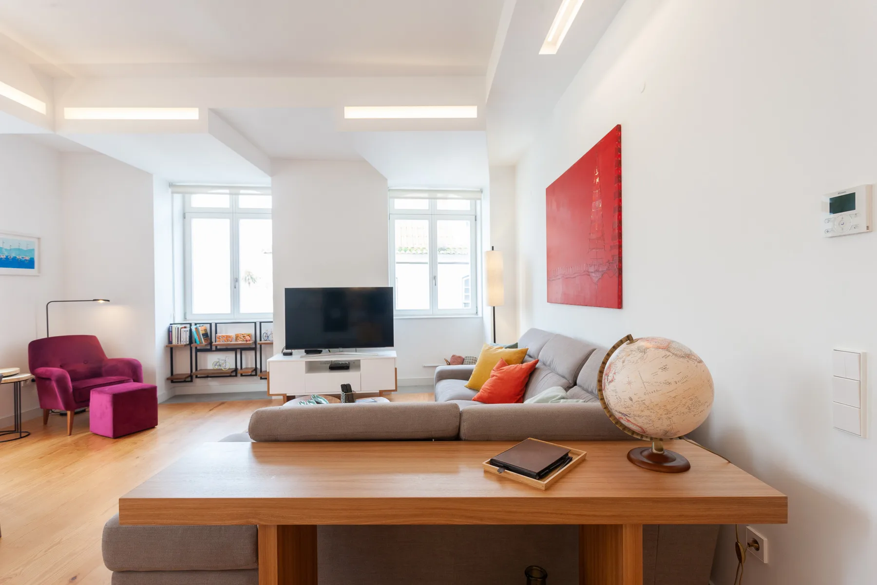 Una sala de estar luminosa con sofá, televisor y grandes ventanas.