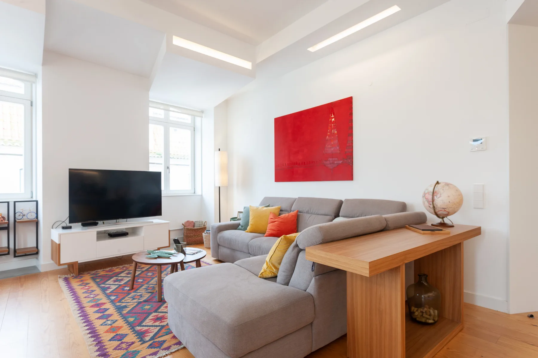 Una sala de estar luminosa con asientos, un televisor y una alfombra colorida.