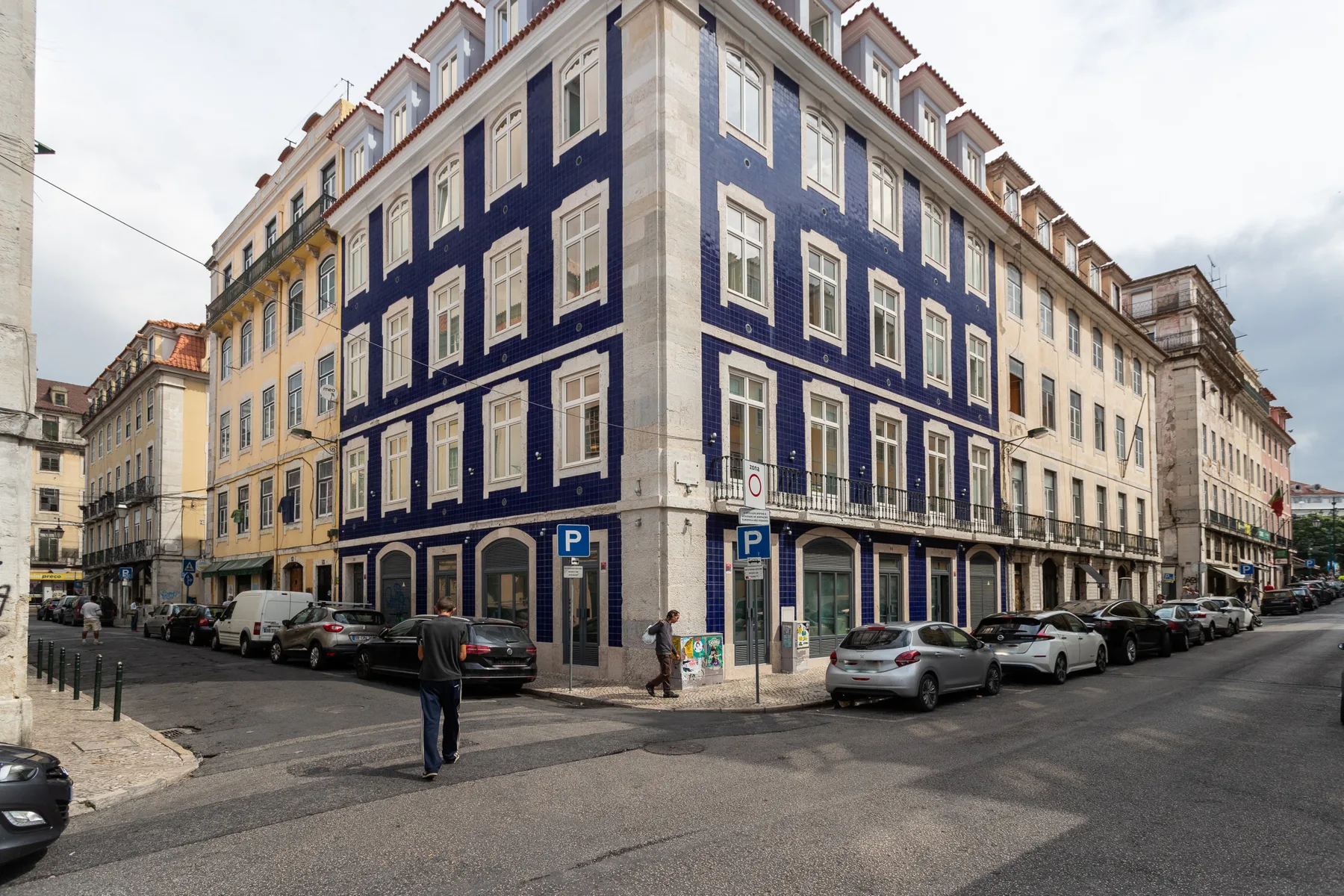 Un edificio azul y blanco en una esquina junto a una calle urbana con coches aparcados.
