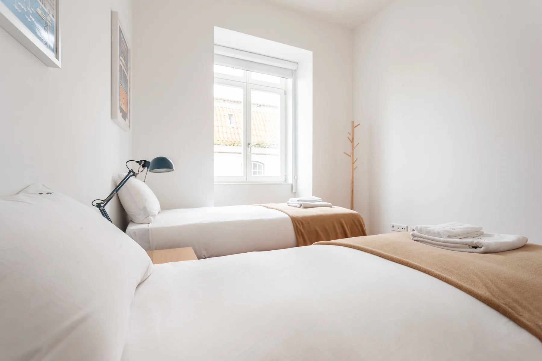 Un dormitorio luminoso con dos camas, sábanas blancas y una ventana.