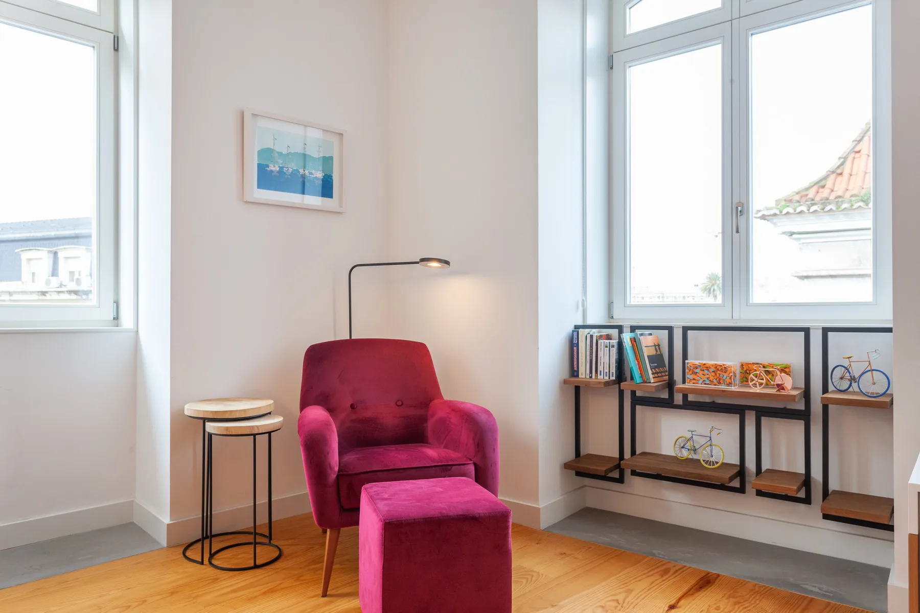 Una luminosa zona de estar tiene un sillón magenta, un reposapiés y ventanas altas.