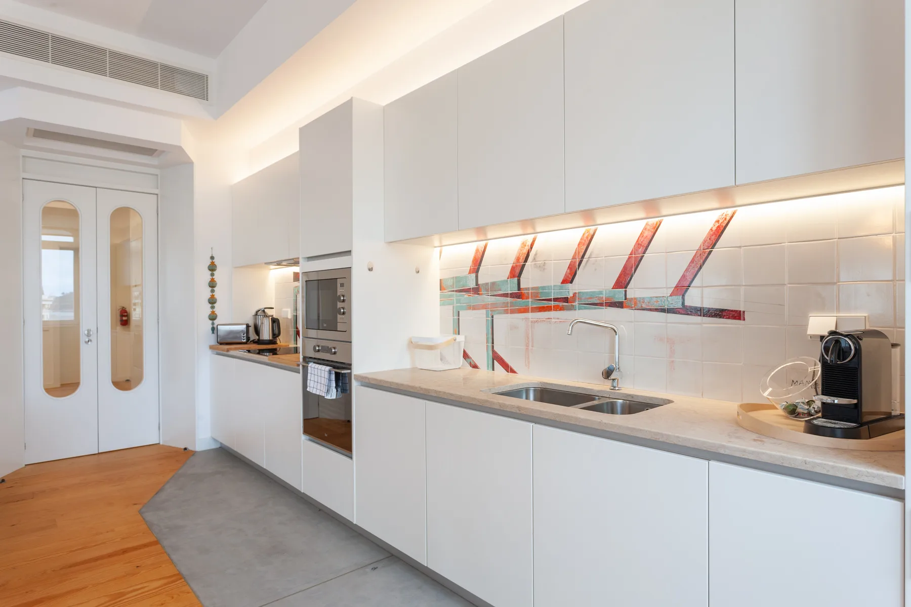 Una cocina moderna con gabinetes blancos, una encimera larga y un horno integrado.