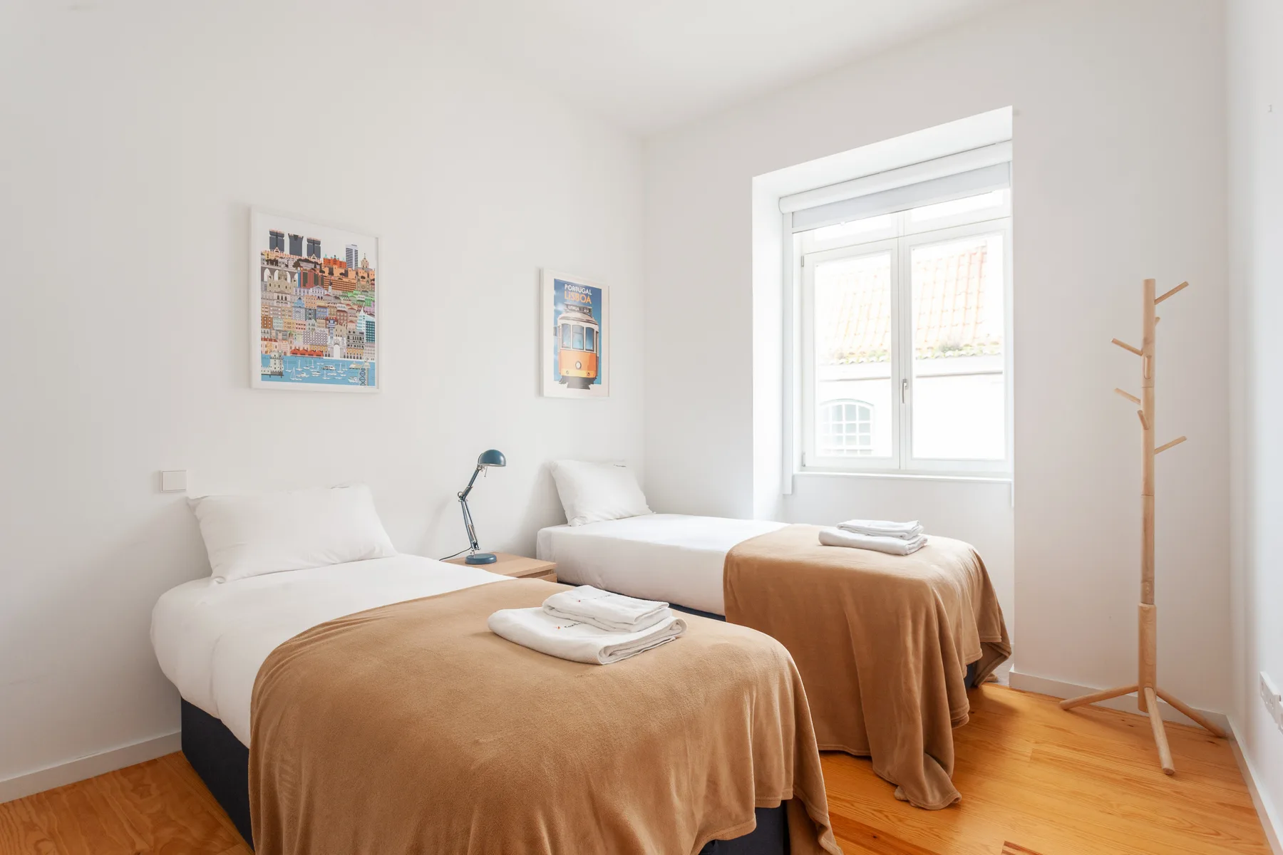 A bright bedroom with two beds dressed in white and tan linens.